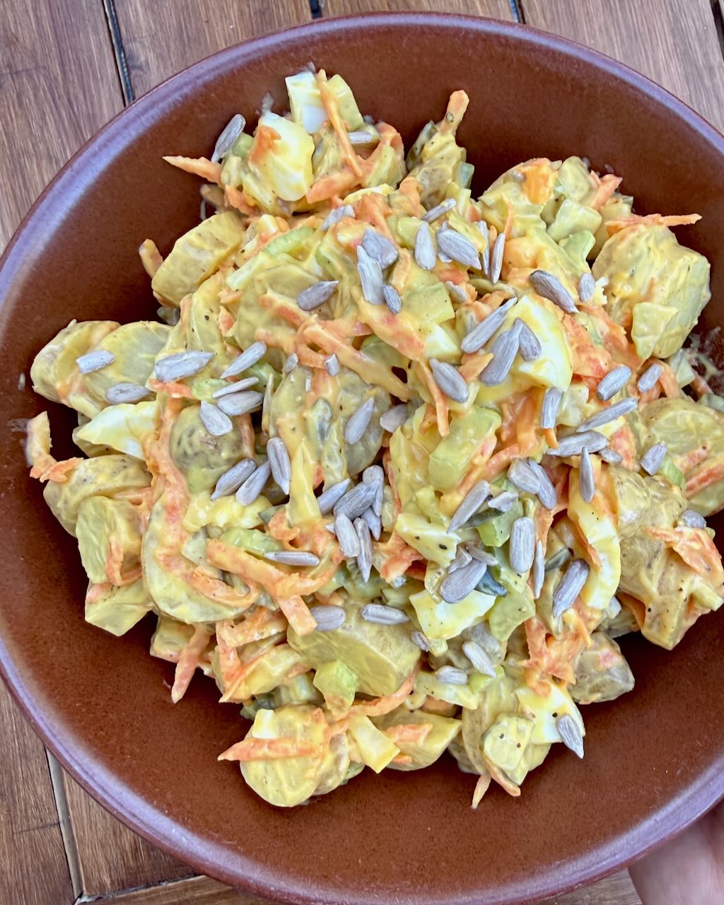 Classic potato salad in a brown bowl on a wooden table.