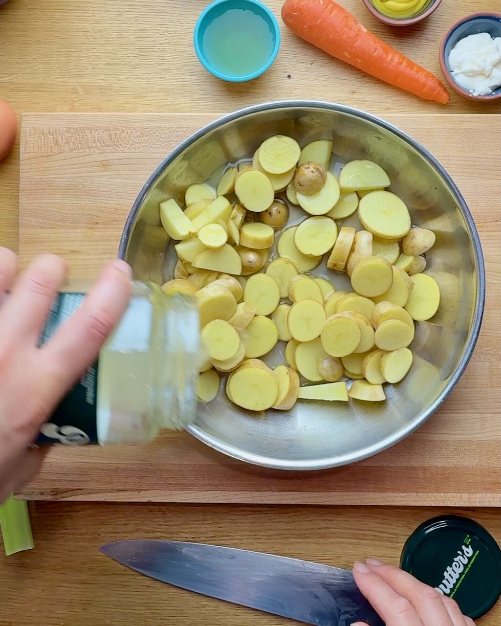 A woman pours pickle juice over sliced potatoes to boil.