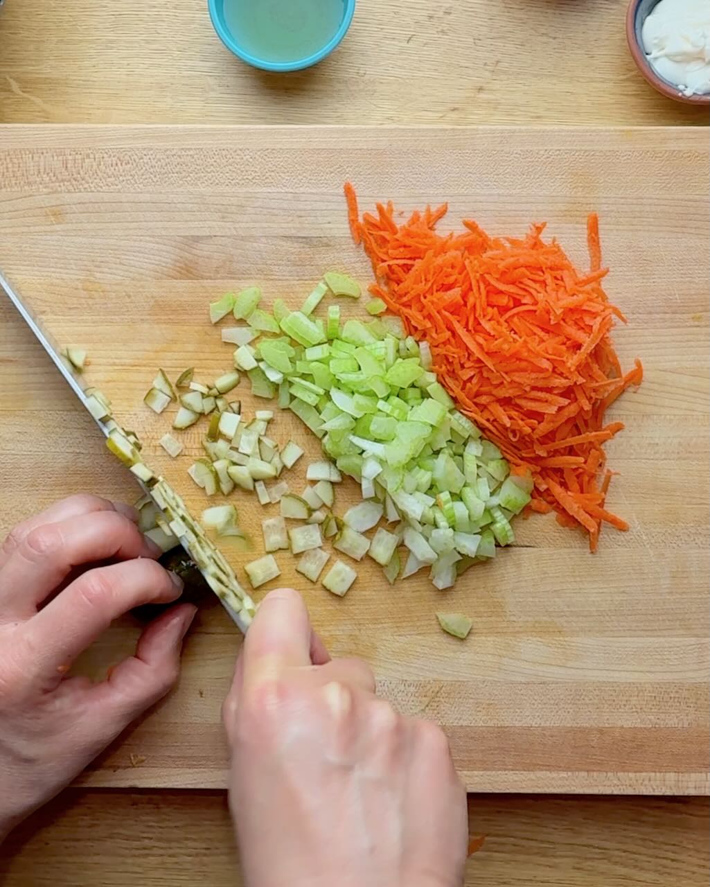 Grated carrots, chopped celery and pickles on a wooden cutting board.
