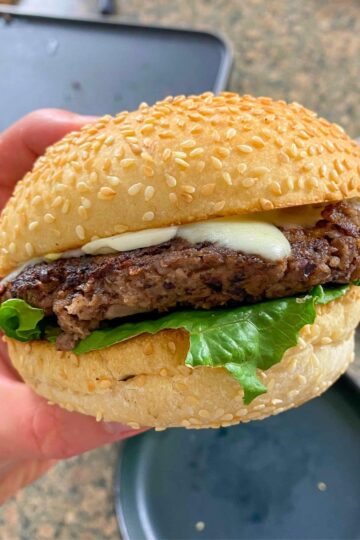 close-up shot of a mushroom walnut veggie burger with lettuce and cheese on a sesame seed bun.
