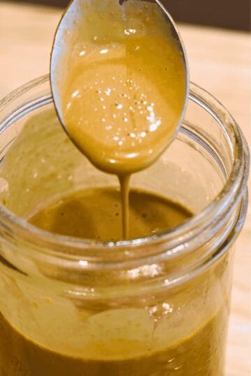 Creamy nutritional yeast dressing dripping off a spoon into a glass jar.