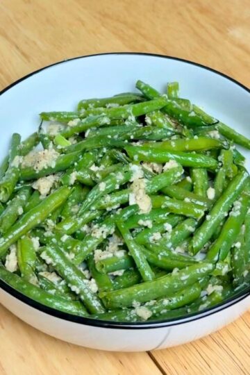 garlic parmesan green beans in a white bowl with lemon wedges on top.