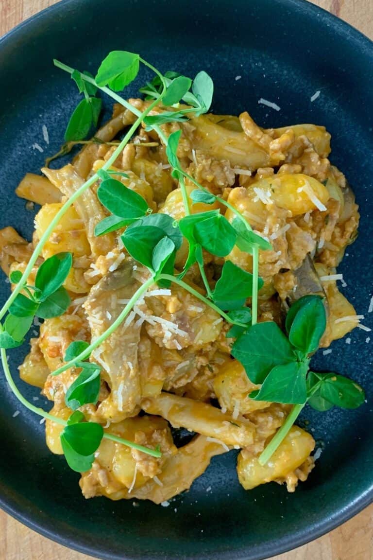 a plate of red pesto gnocchi with pea shoots on top.