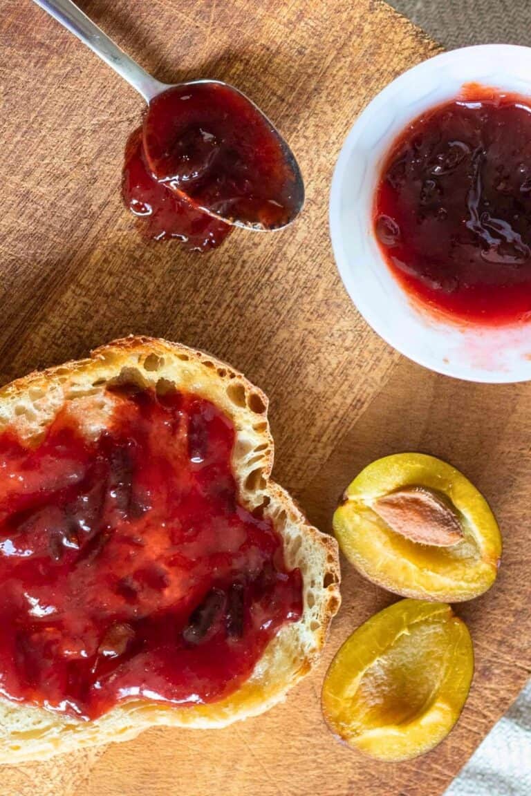 Plum and ginger jam on toast with a cut fresh plum next to it.