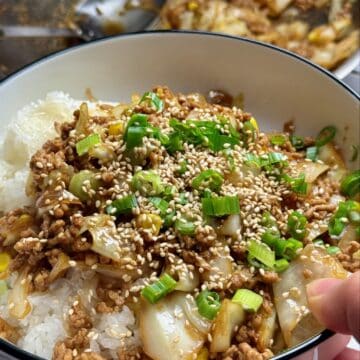 A woman holds pork and cabbage stir fry over rice in a white bowl with black trim.