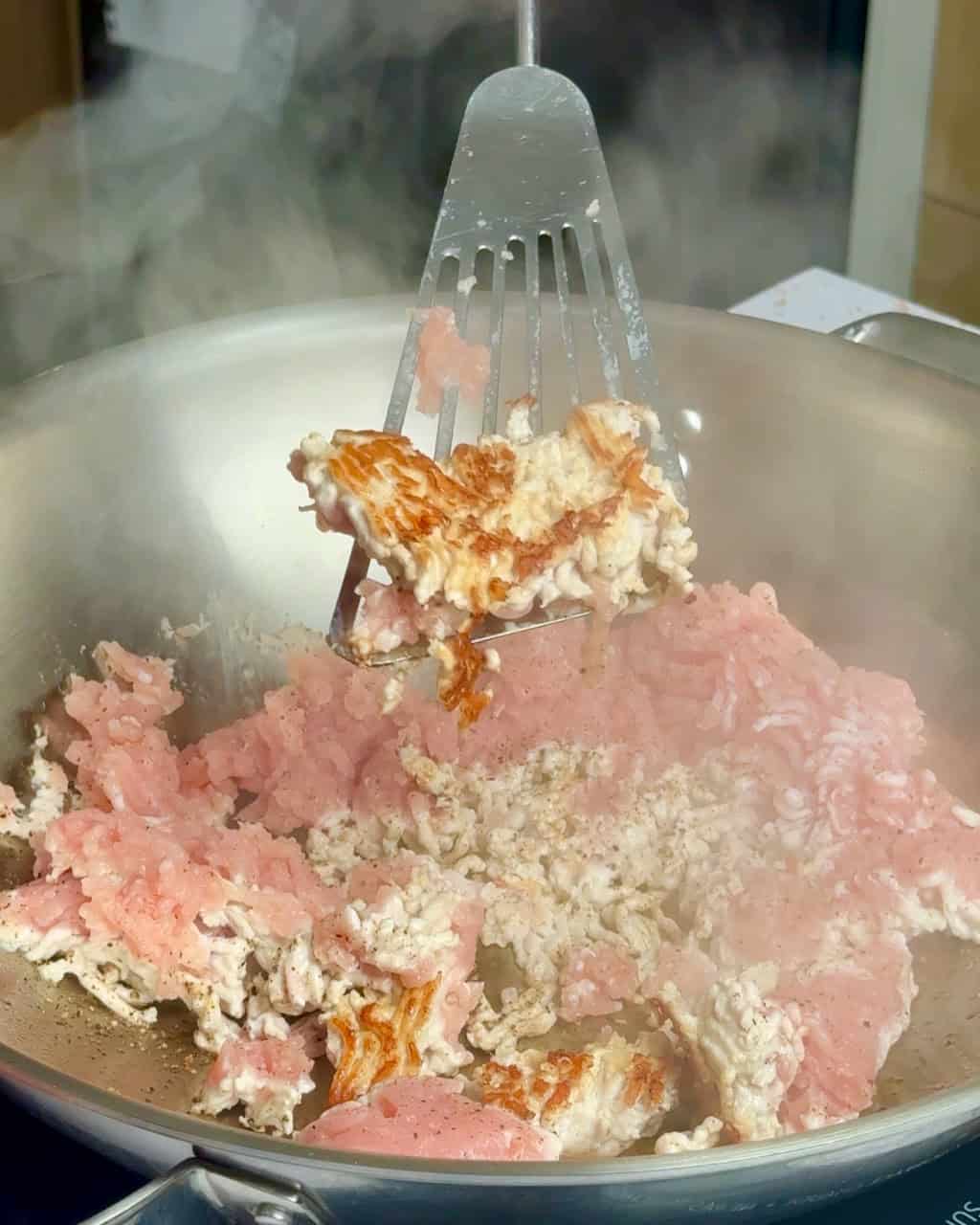 An image of ground pork browning in a stainless steel wok.