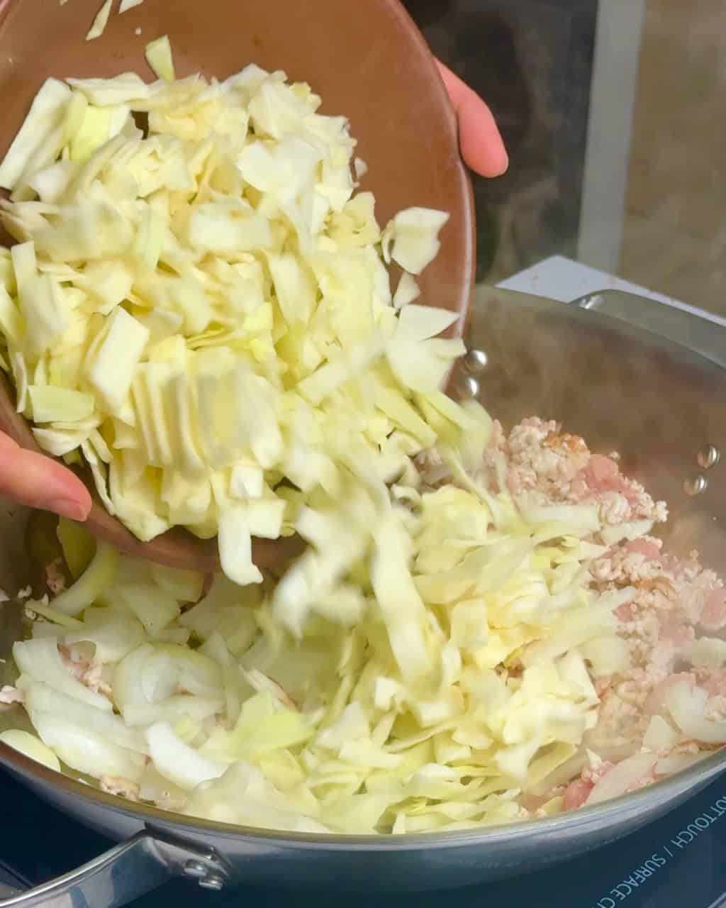 A woman adds the chopped cabbage to the pork and onions.