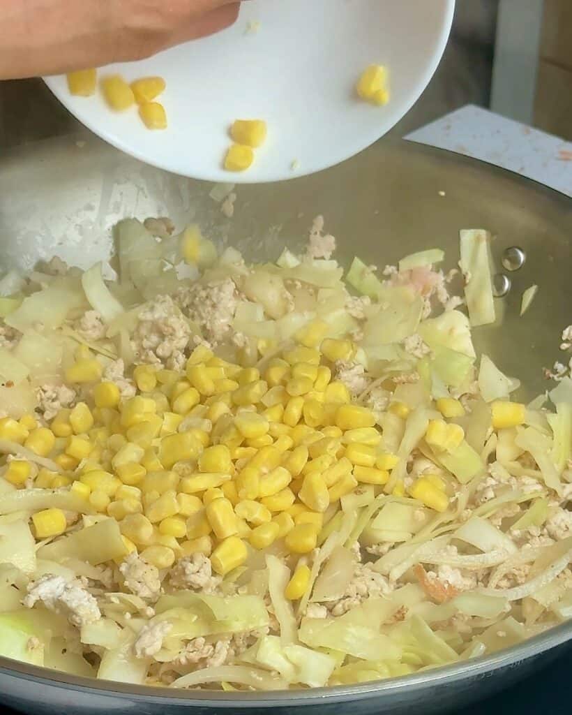 Adding frozen corn to the stir fry.