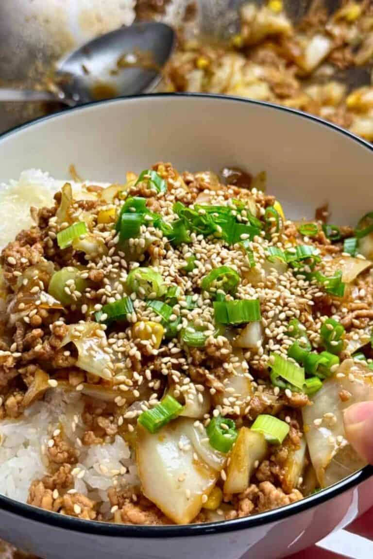A woman holds pork and cabbage stir fry over rice in a white bowl with black trim.
