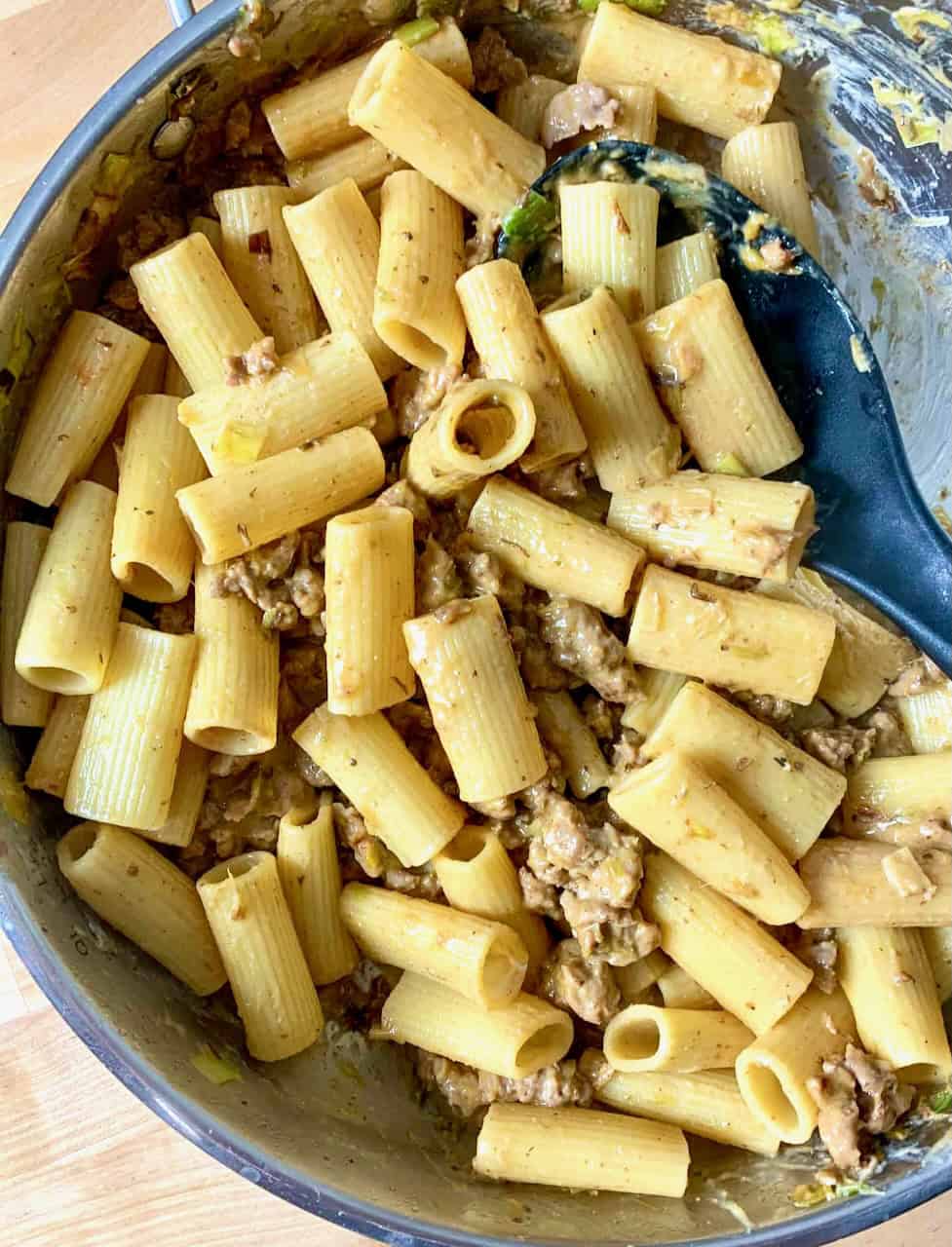 Scooping a portion of creamy sausage and leek pasta from a pan.