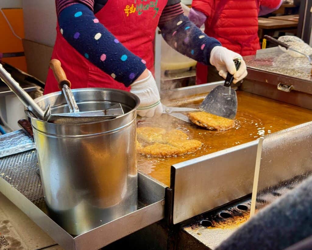 A woman fries mung bean pancakes in plenty of oil on a hot griddle in Gwangjang market.