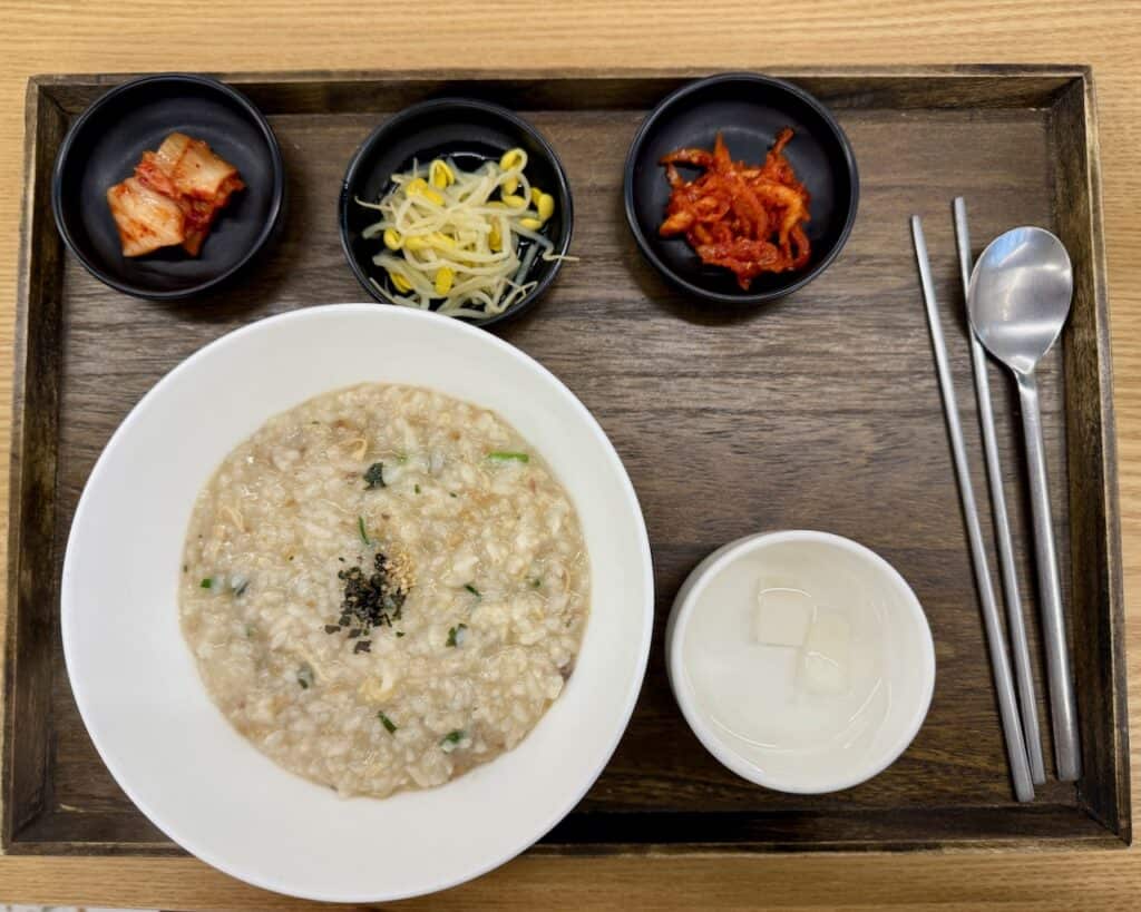 A place setting with a bowl of chicken porridge (dakjuk) with side dishes (banchan).