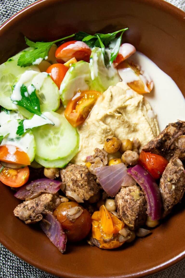 A chicken shawarma bowl with lemon wedges and pickled beets on the side.