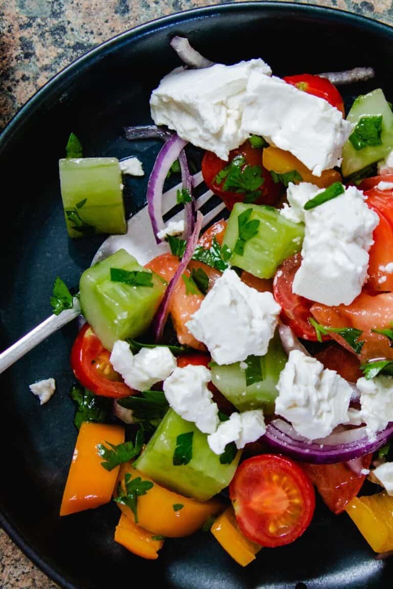 Bulgarian Shopska Salad in a blue bowl with some red onion an cherry tomatoes on the side.
