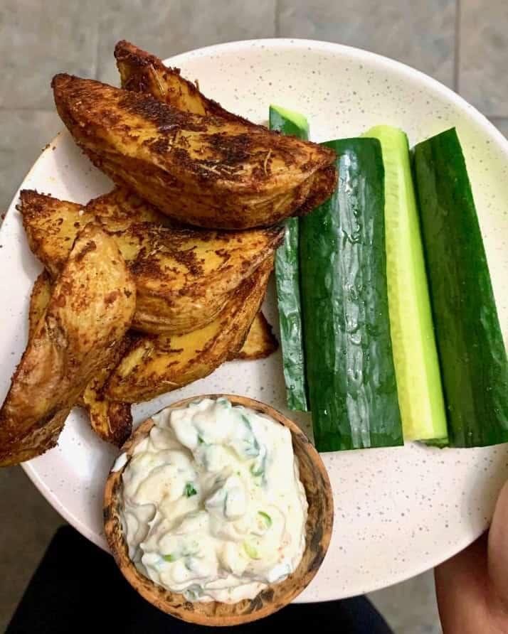 A snack plate with roasted potato wedges, cucumber sticks, and sour cream and onion dip.