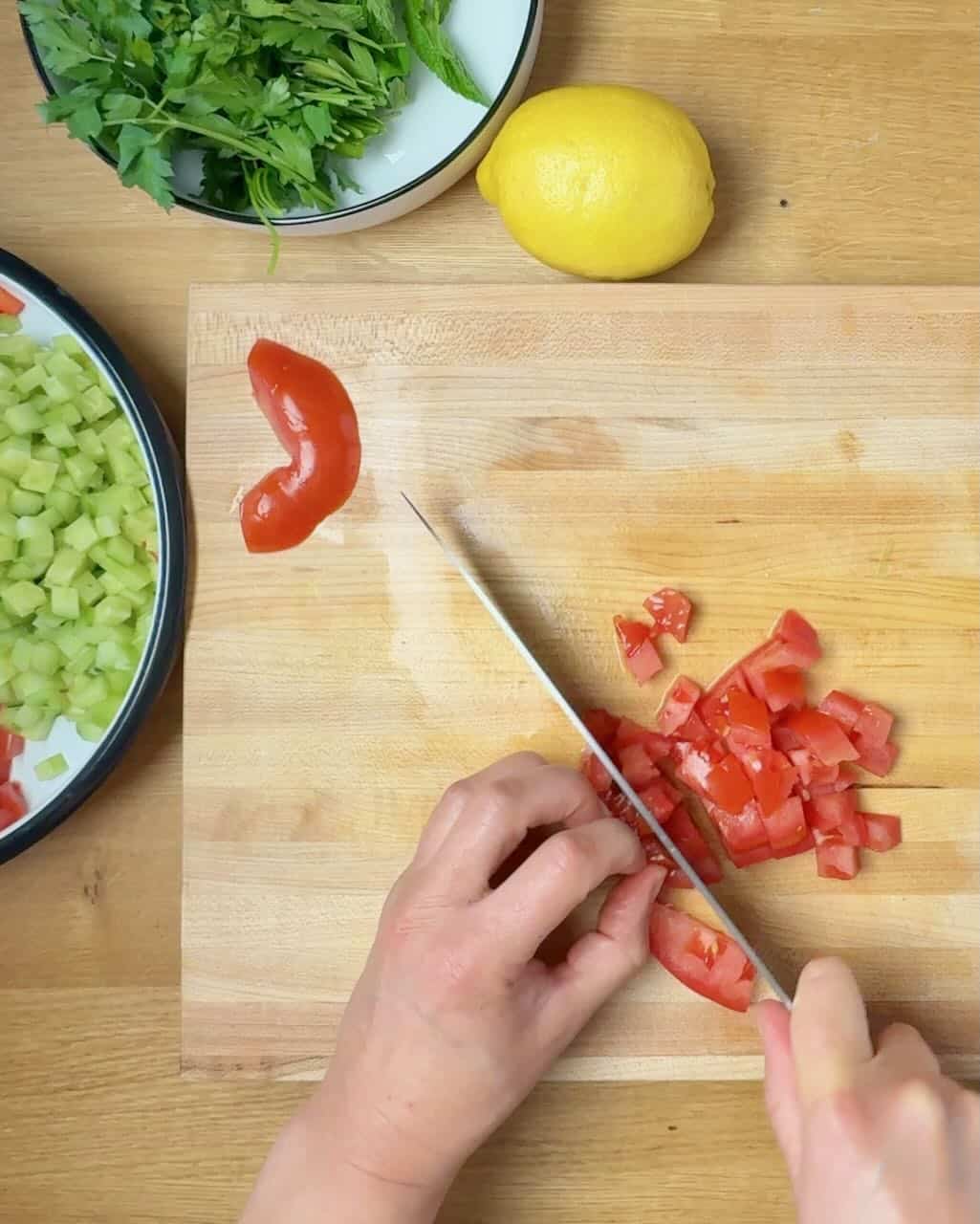 A woman chops fresh tomato on a wooden cutting board.