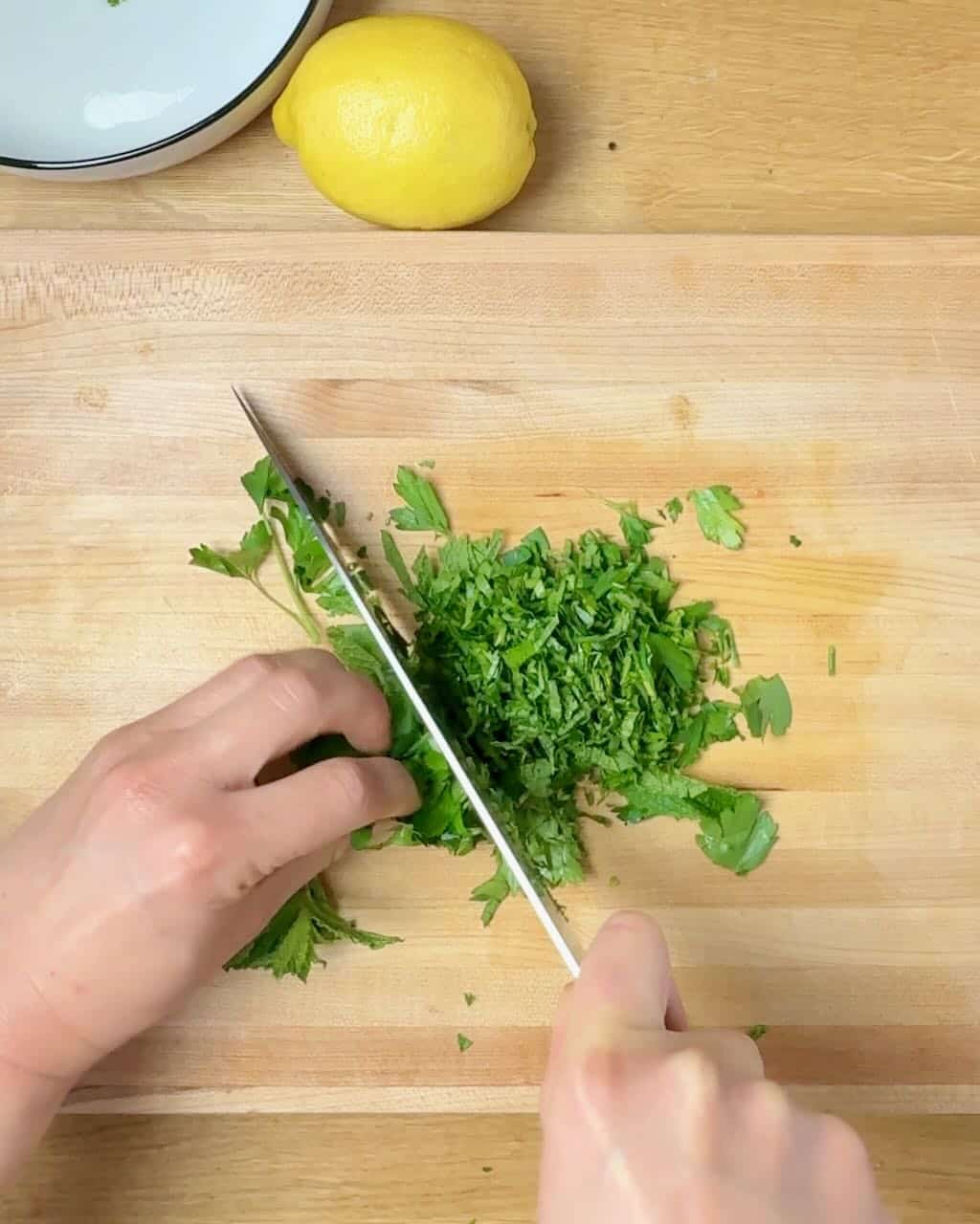 A woman chops fresh parsley and mint on a wooden cutting board.