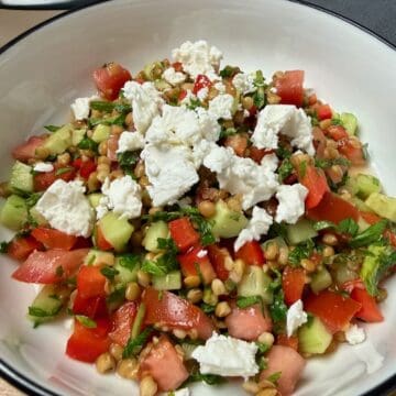 Summer Lentil Salad with feta cheese, tomatoes, cucumbers, and herbs in a white bowl.