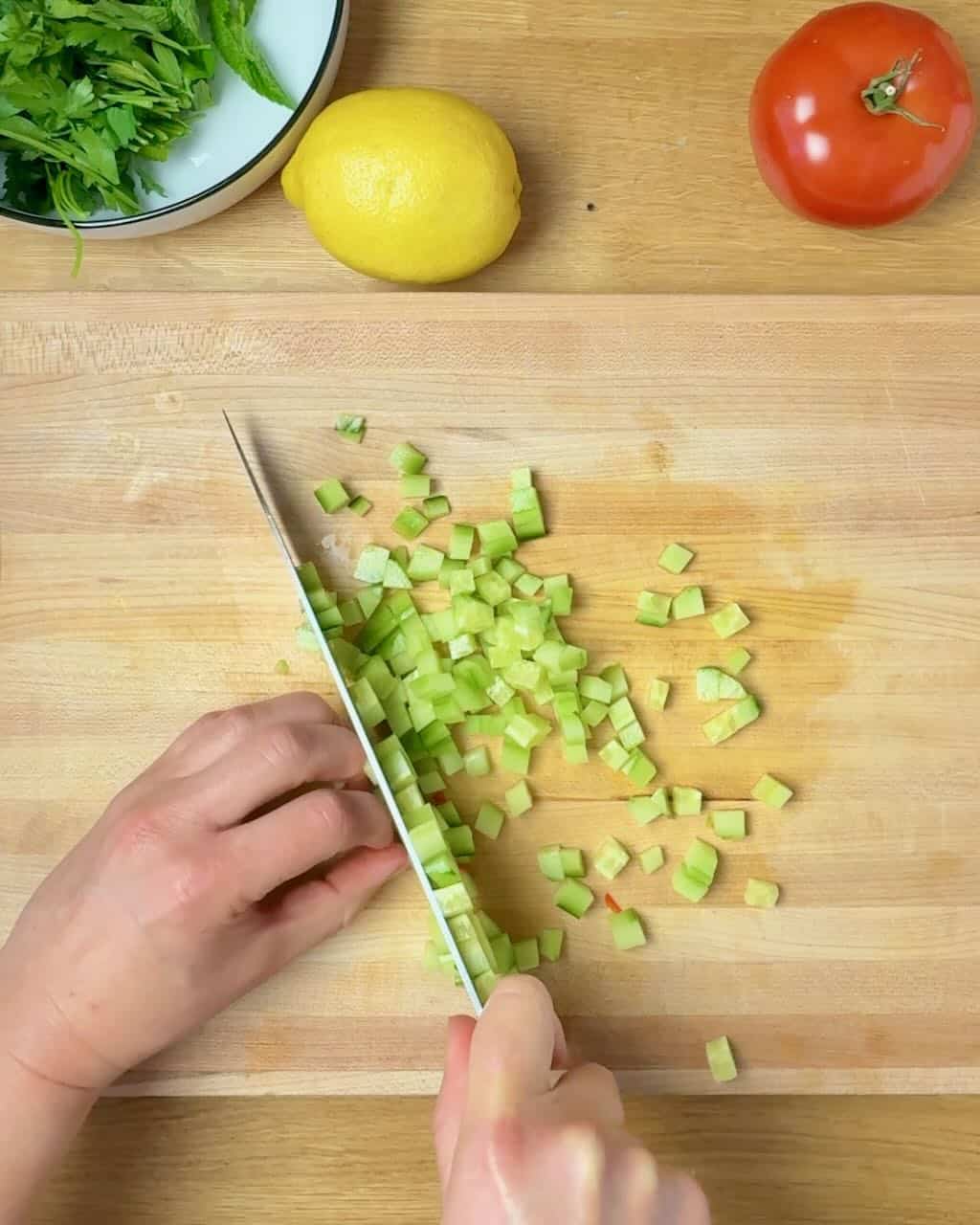 A woman chops cucumber on a wooden cutting board.
