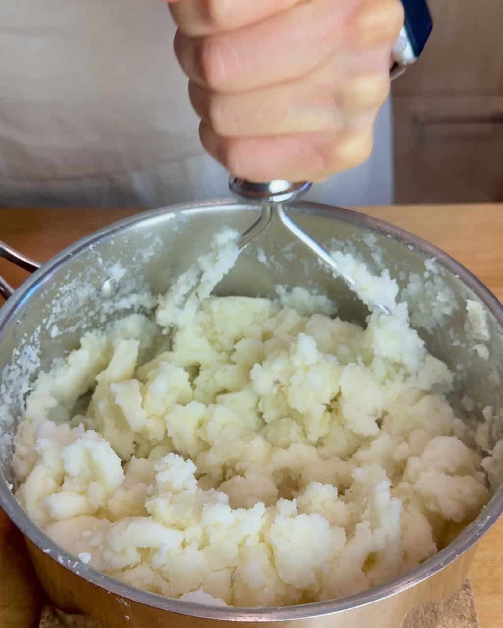 A woman mashes potatoes in a pot.