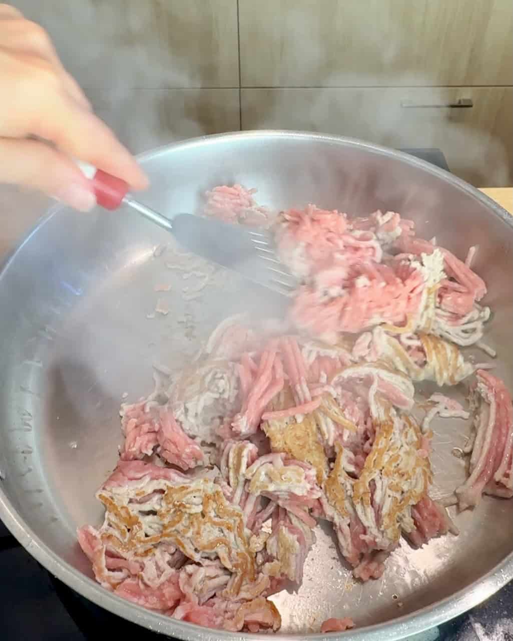 Browning ground turkey in a stainless steel skillet.