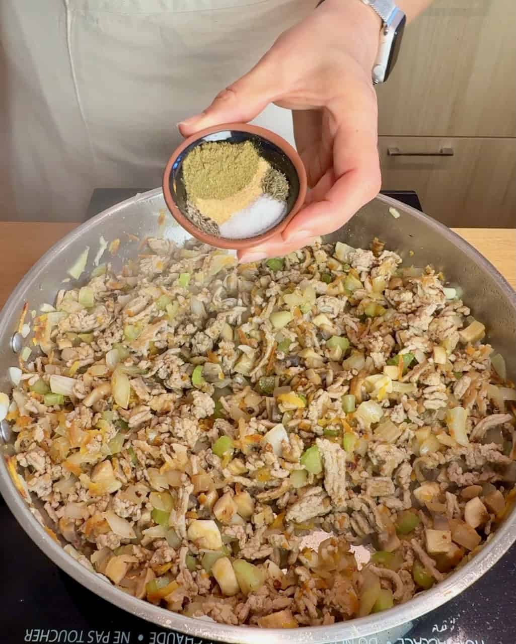 A woman adds spices to the turkey vegetable mixture.