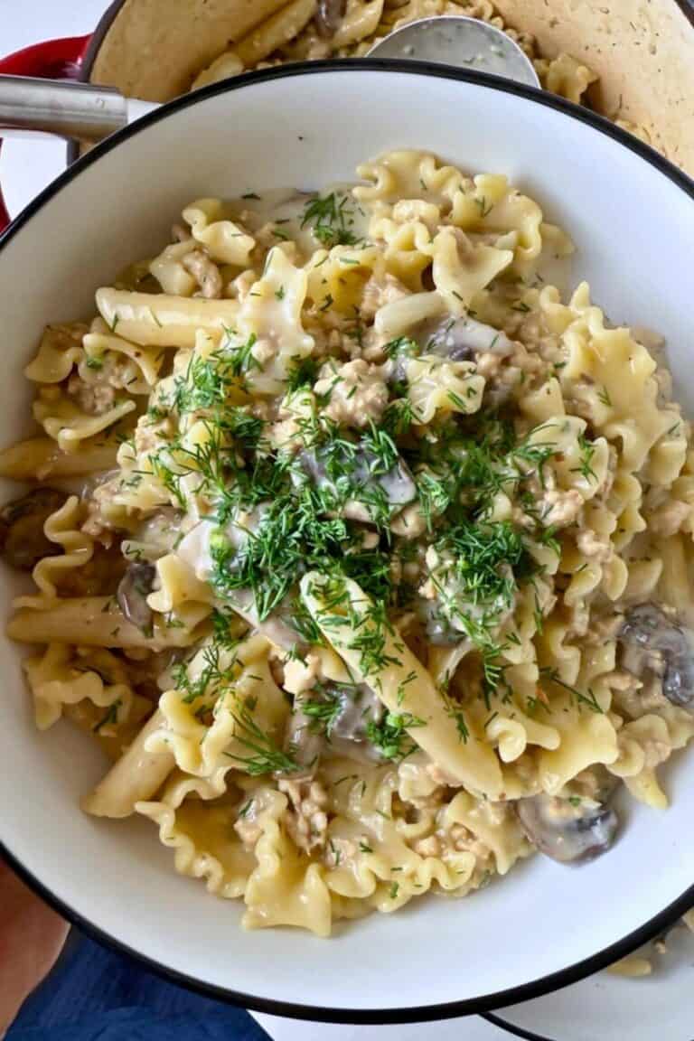 A woman holding a bowl of stroganoff topped with fresh dill.