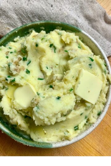 Closeup of a spoonful of mashed potatoes with a bowl of mashed potatoes in the background.