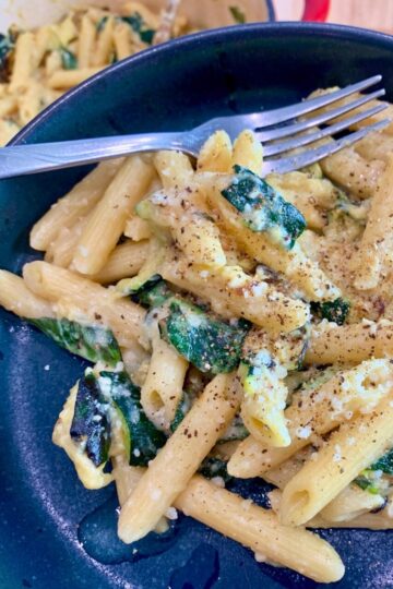 Creamy zucchini pasta with half a lemon on the side, on a dark blue plate with a fork.
